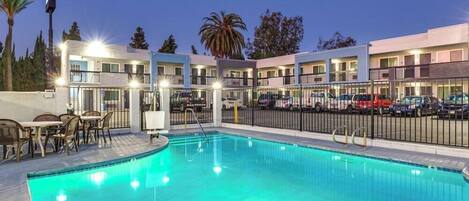 A hotel with a swimming pool, outdoor seating, and multiple balconies.