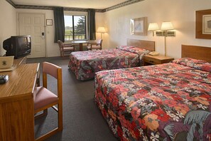 Habitación de hotel con dos camas, un escritorio, una silla, un televisor y una ventana con cortinas.