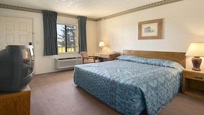 Una habitación de hotel con cama, escritorio, silla, televisor y ventana con cortinas.