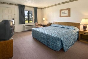 Una habitación de hotel con cama, escritorio, silla, televisor y ventana con cortinas.