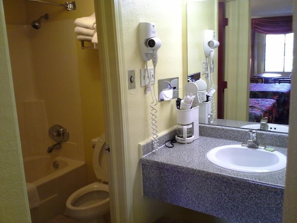 Un baño con bañera, inodoro y lavamanos. Hay dos secadores de pelo montados en la pared.