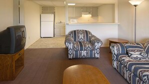 Una sala de estar con televisor, sillón estampado, sofá y una mesita. Se ve una cocina al fondo.