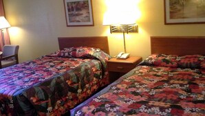 Una habitación de hotel con dos camas, cada una con ropa de cama floral, una mesita de noche con lámpara y un cuadro en la pared.