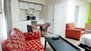 Ett hotellrum med en röd soffa med mönster, ett svart bord, en liten köksdel med mikrovågsugn och två stolar.