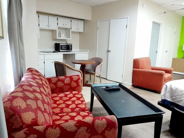 A hotel room with a red patterned sofa, a black table, a small kitchen area with a microwave, and two chairs. - Budgetel Inn and Suites Fort Gordon Augusta (Augusta)