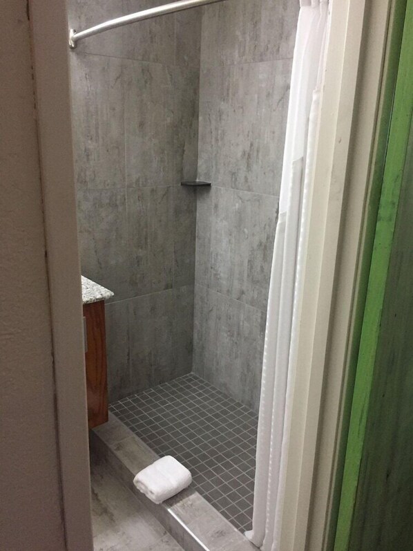 A small, enclosed shower area with a tiled floor and a white towel on the step.