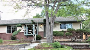 A two-story house with a brick facade, a number '3613' on the front, and a well-maintained garden with a tree and shrubs. - Serendipity House (Colorado Springs)