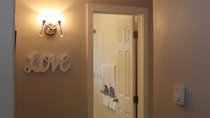 A bathroom with a towel rack, a wall-mounted light fixture, and a thermostat. - Serendipity House (Colorado Springs)