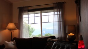 A living room with a couch, a lamp, a lava lamp, and a view through a window. - Serendipity House (Colorado Springs)