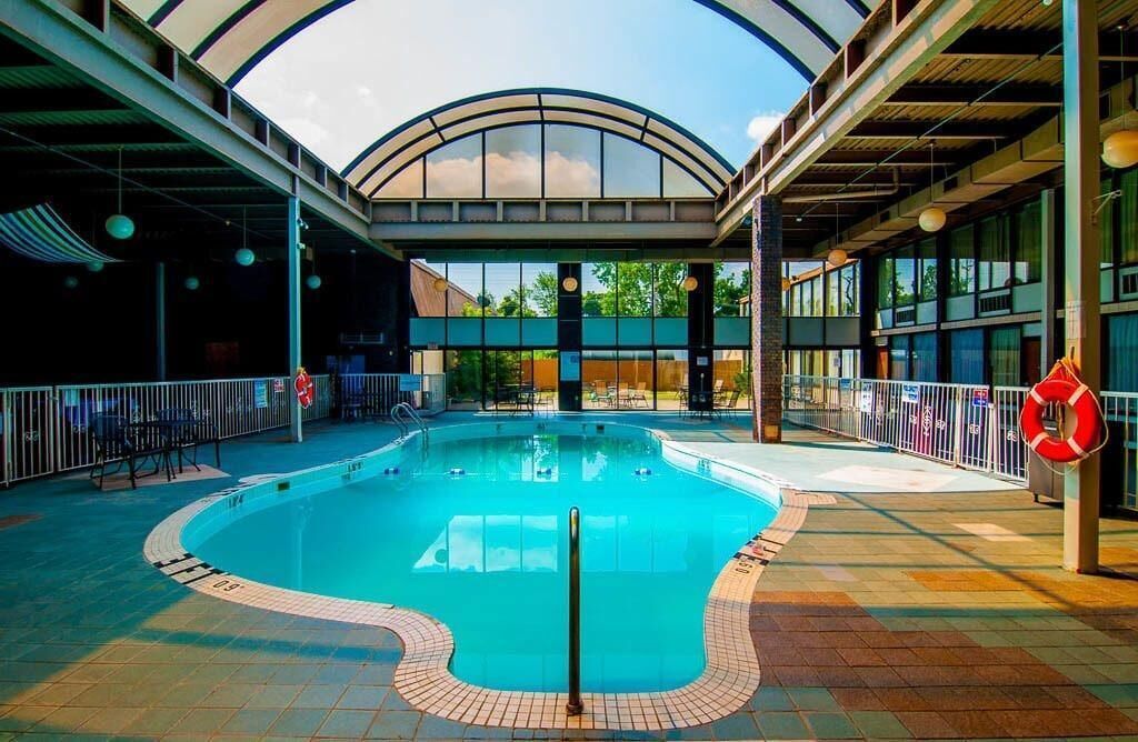 Une piscine intérieure au design incurvé, entourée d’un sol carrelé et protégée par une paroi en verre.