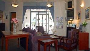 Eine Hotellobby mit einer Couch, Sesseln, einem Couchtisch, einem Fernseher und einer Rezeption.
