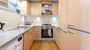 A compact kitchen with wooden cabinets, a built-in oven, a stainless steel range hood, and a countertop with a sink. - Broompark (Glasgow)