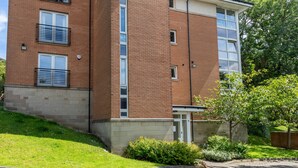 A multi-story brick building with balconies, a small garden area, and a paved entrance. - Broompark (Glasgow)