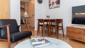 A modern living room with a black leather chair, a dining table with four chairs, a TV on a wooden cabinet, and a book on a marble table. - Broompark (Glasgow)