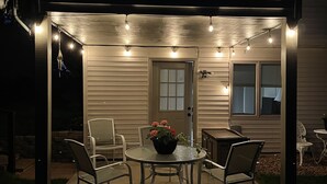 An outdoor patio area with a table and chairs, string lights, and a potted plant.