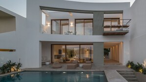 Een modern huis met twee verdiepingen, een zwembad, buiten zitplaatsen en een balkon.