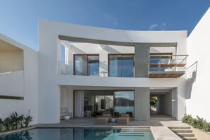 Une maison moderne à deux étages, dotée d’une piscine, de grandes fenêtres et d’un balcon.