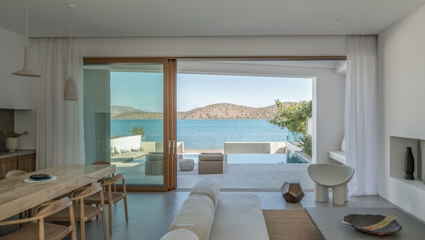 Een moderne woonkamer met een grote schuifpui naar een balkon met uitzicht op water en heuvels.