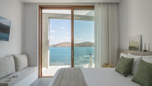 Een hotelkamer met een groot bed, een slaapbank, een balkon met uitzicht op zee, en een kleine tafel met een stoel.