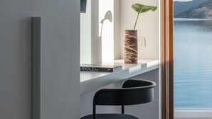 Een modern interieur met een minimalistisch design, met een zwarte stoel, een witte plank met een plant en uitzicht op de zee door een groot raam.