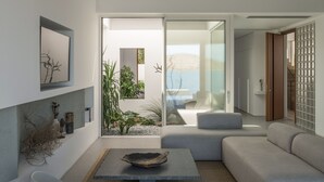 Een moderne woonkamer met een stenen tafel, een grijze bank en uitzicht op een tuin en water.