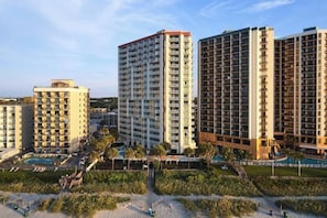 A high-rise hotel with multiple floors, a swimming pool, and a landscaped area with palm trees.