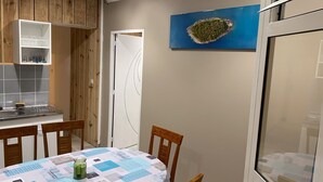 Une cuisine avec des meubles en bois, un pare-feu en carreaux, une table à manger avec des chaises et un tableau accroché au mur.