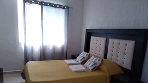 A neatly made bed with a yellow bedspread and two pillows, a headboard with a tufted design, and a nightstand with a black drawer. - Casa Gueza (Benito Juarez)