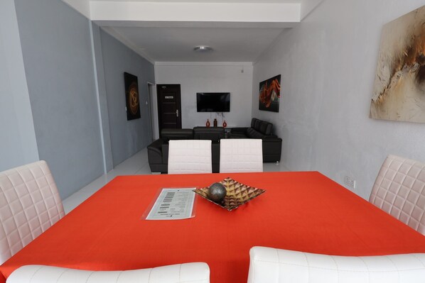 A modern dining area with a red tablecloth, white upholstered chairs, and a black and white sofa in the background. - Luxury 3BD Villa Located in Rodney Bay (Gros Islet)
