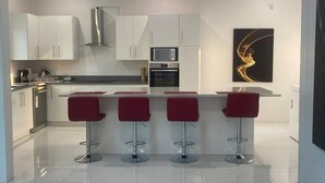 Cozinha moderna com armários brancos, coifa de aço inoxidável, micro-ondas e forno. Há quatro banquetas vermelhas na ilha.