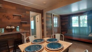 Un comedor con una mesa de madera dispuesta para cuatro personas, un sofá y una barra de café con estanterías.