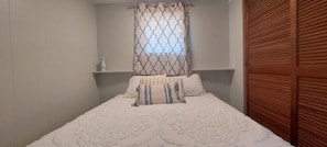 Un dormitorio con una cama, una ventana con cortinas estampadas, un estante con una botella y una puerta de madera.