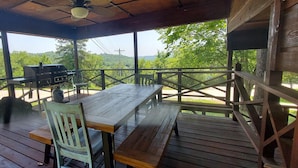 Un patio techado al aire libre con una mesa y sillas de madera, una parrilla y vistas a la vegetación circundante.