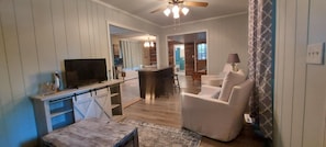A modern living room with a TV, a dining area, and a kitchen in the background.