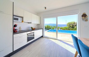 A modern kitchen with a view of a swimming pool and mountains.