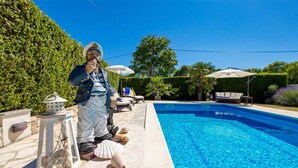 Ein Schwimmbad mit einer Statue eines Seemanns, der ein Teleskop hält, umgeben von Gartenmöbeln und einem gepflegten Garten.