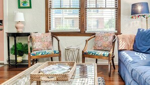 A cozy living room with a blue sofa, two wooden chairs with floral cushions, a glass coffee table with magazines, and a small side table with a lamp. - The Funky Swan Shack by Lake Morton & Downtown (Lakeland)