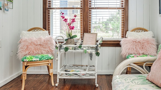 A cozy room with two wicker chairs, a small white metal cart, and a bed with floral bedding. - The Funky Swan Shack by Lake Morton & Downtown (Lakeland)