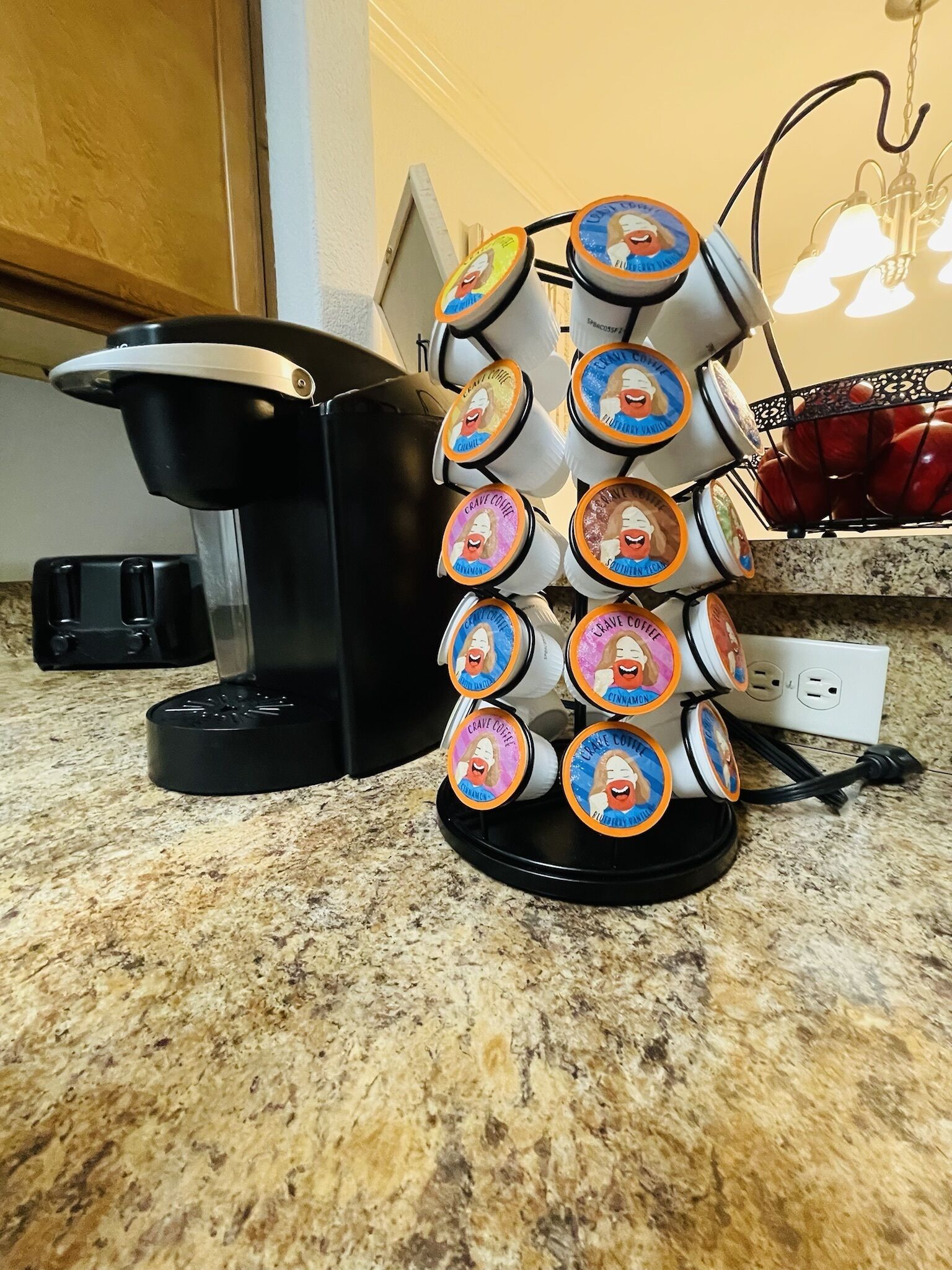 Een keuken met een koffiezetapparaat, een fruitmand en een stroomstrip aan de muur.