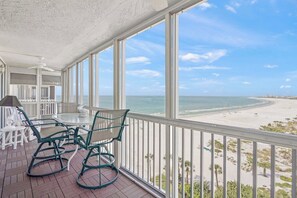 Een balkon met een tafel en stoelen, met uitzicht op een strand.