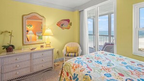 A bedroom with a bed, a dresser, a chair, a window with a view of the beach, and a large mirror. - Crystal Sands Tower Unit 1007 - Beachfront (Sarasota)