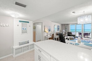 A modern kitchen with a large island, a dining area with a view of the ocean, and a living room with a beach-themed decor. - Crystal Sands Tower Unit 204 - Beachfront (Sarasota)
