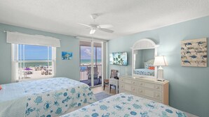Un dormitorio con dos camas, un aparador, una silla, un ventilador de techo y vista a la playa.