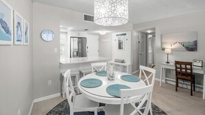 Una cocina moderna con armarios blancos, un refrigerador de acero inoxidable y un comedor con sillas blancas y una mesa redonda.