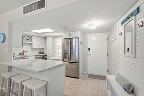 A modern kitchen with a central island, stainless steel appliances, and a white color scheme. - Crystal Sands Tower Unit 204 - Beachfront (Sarasota)