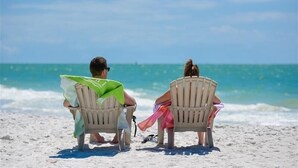 Zwei Personen sitzen auf Strandliegen und blicken auf den Ozean.