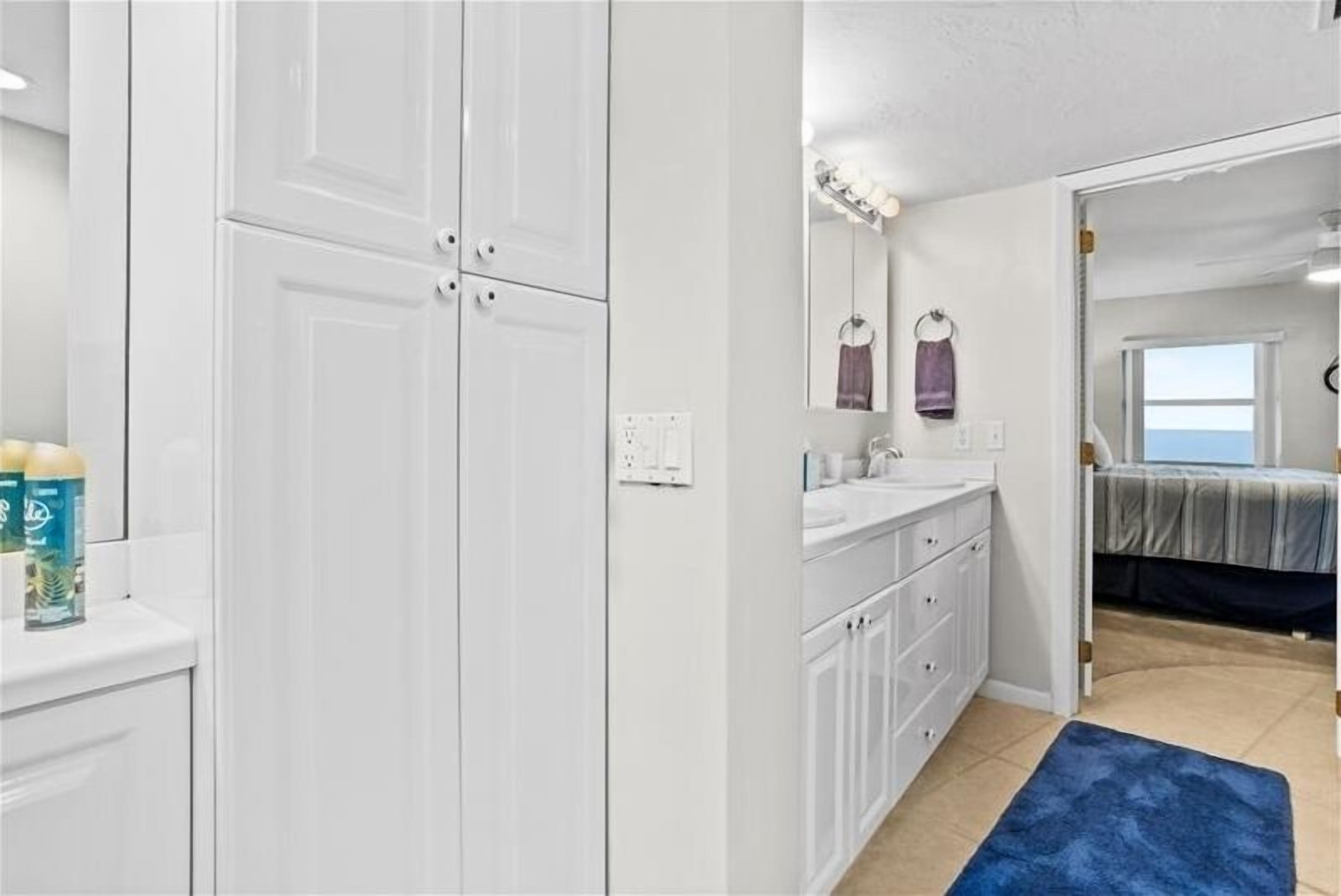 A bedroom with a bed, a window, and a bathroom with a sink and cabinets.