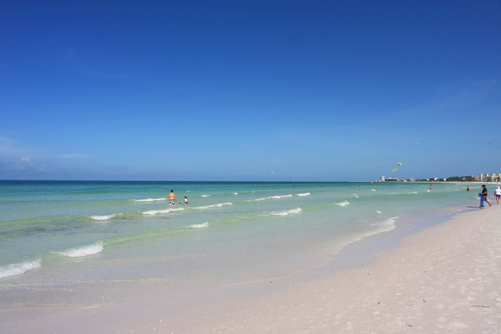 A beach with clear blue water, a sandy shore, and a few people in the distance.