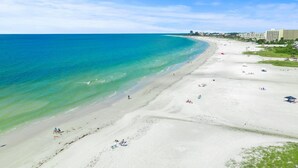 A wide sandy beach with clear turquoise waters, a few people, and buildings in the background. - Crystal Sands Tower Unit 909 - Beachfront (Sarasota)