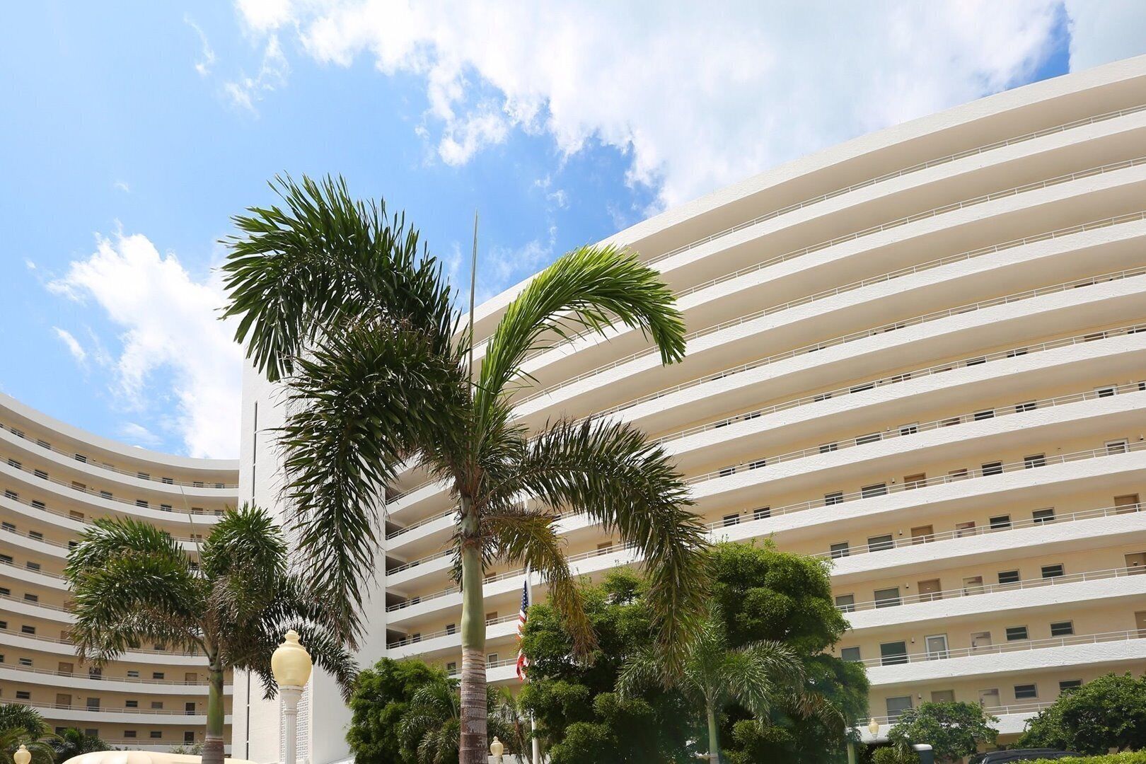A multi-story hotel with a curved facade, palm trees, and a clear blue sky.